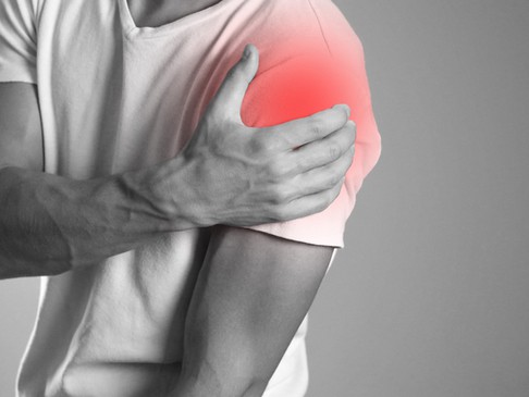 A man holds his deltoid muscle, where an area of pain is depicted in red