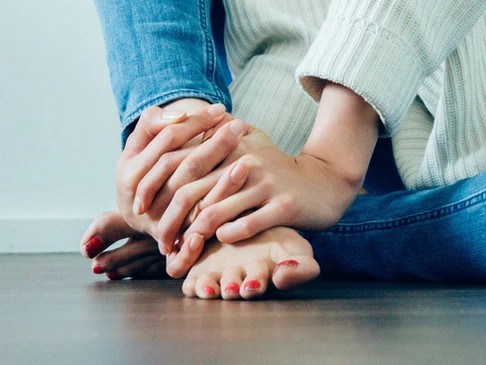 A woman sits on the floor with hands wrapped around her ankle