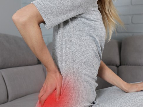 A woman sits on the couch holding an area of pain in the lower back