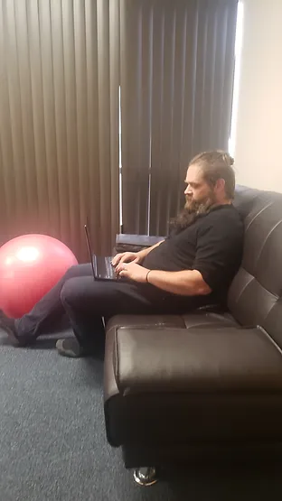 David works on a laptop on a couch to demonstrate how this sitting position can cause lower back pain