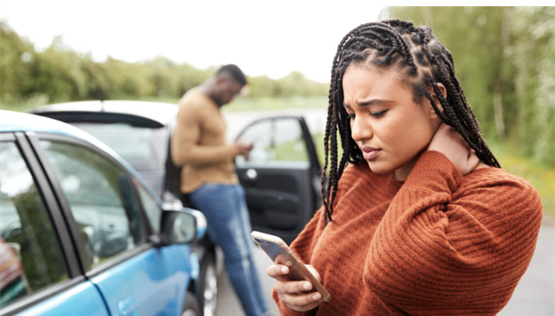 Woman experiencing neck pain after a car accident, looking at phone for help
